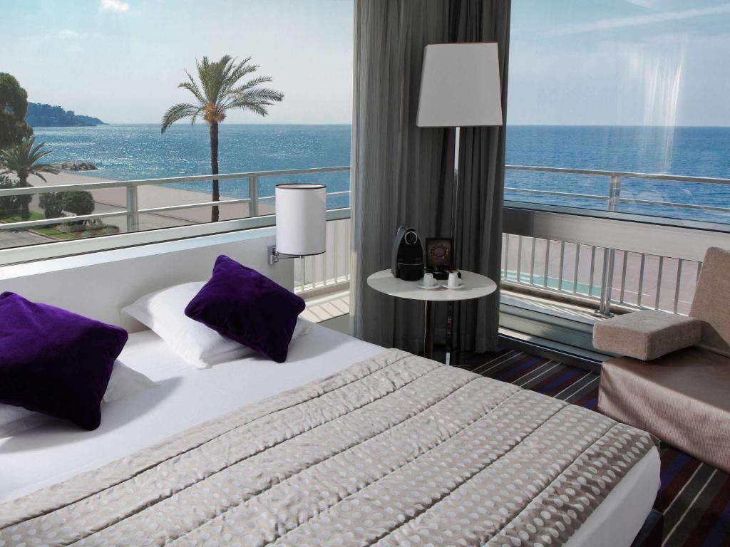 ニースにあるメルキュール ニース プロムナード デ ザングレのベッド付きのホテルルームで、海の景色を望めます。