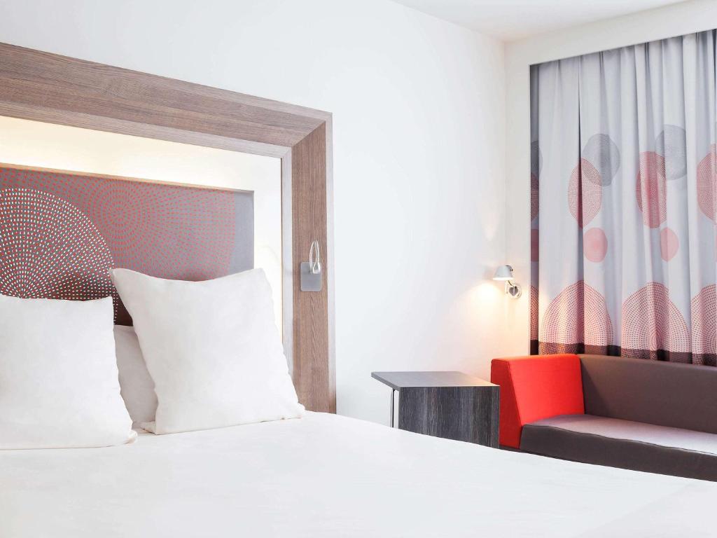 a bedroom with a bed and a red chair at Novotel Lille Aéroport in Lesquin