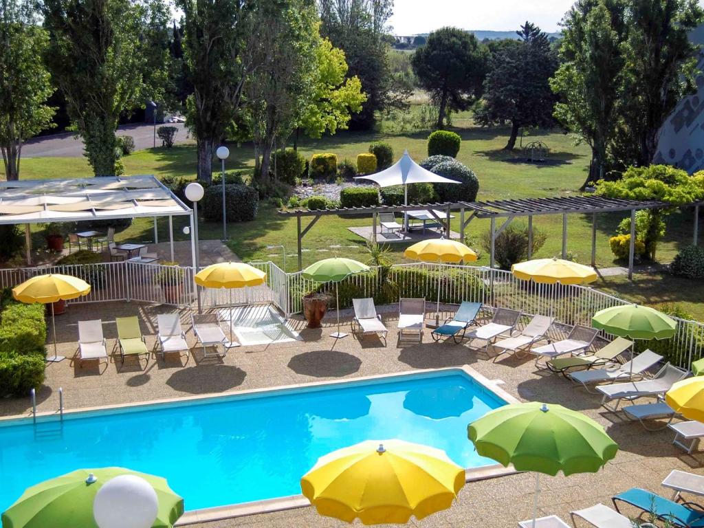 una vista sul soffitto di una piscina con ombrelloni e sedie di ibis Styles Marseille Aéroport a Vitrolles