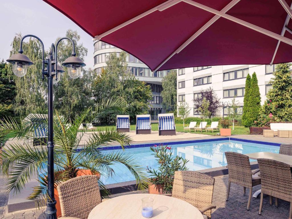 a table with an umbrella next to a swimming pool at Mercure Hotel Frankfurt Eschborn Ost in Eschborn
