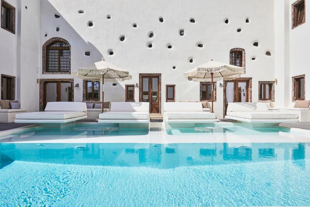 una gran piscina con muebles y sombrillas blancas en Winery Hotel 1870 en Fira