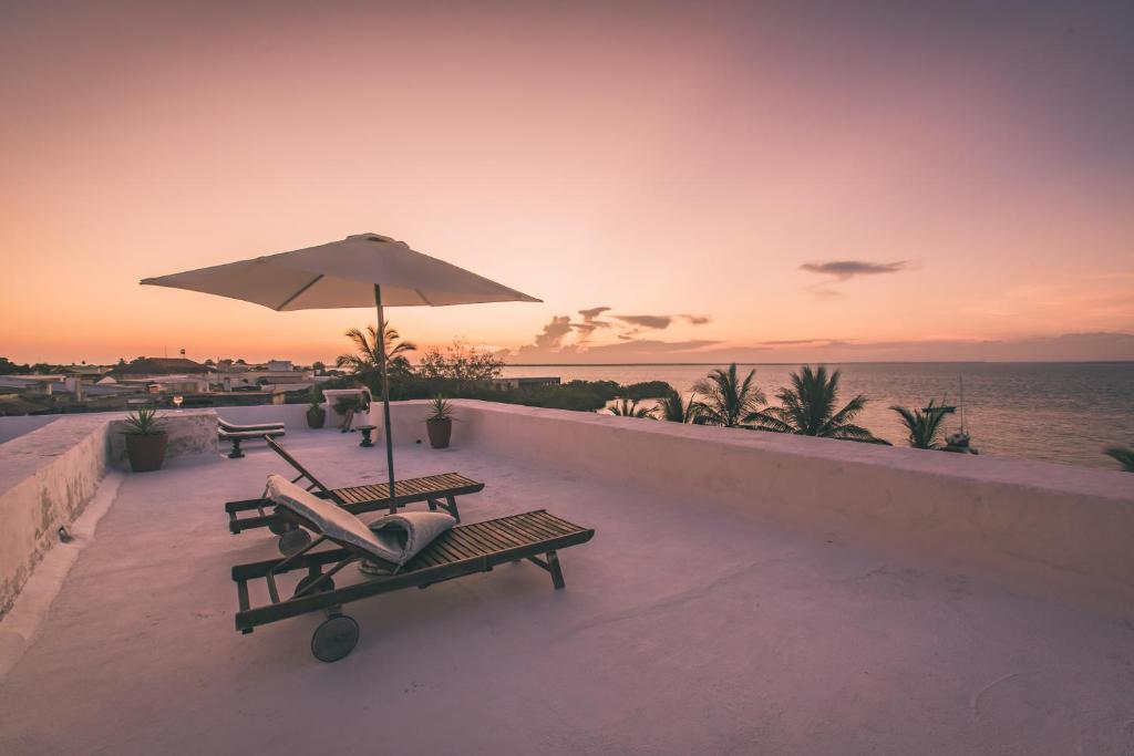a patio with two benches and an umbrella and the ocean at Terraço das Quitandas Design Accommodation-AL in Ilha de Moçambique