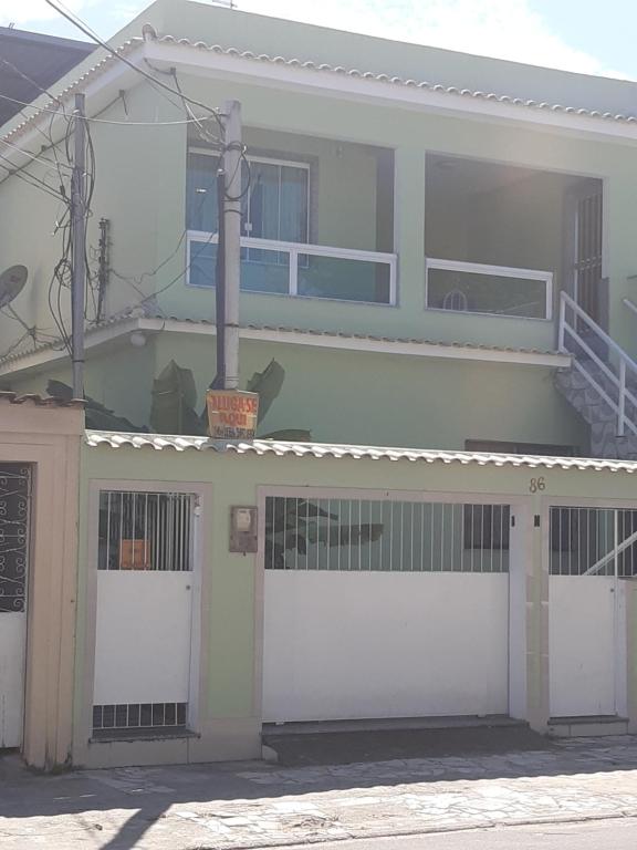 une maison blanche avec deux portes de garage et un balcon dans l'établissement Quarto com banheiro para solteiros no Rio de Janeiro, à Rio de Janeiro