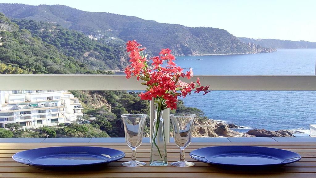 a table with two glasses and a vase with red flowers at ⭑ Sea views + private beach. What else? ⭑ in Tossa de Mar