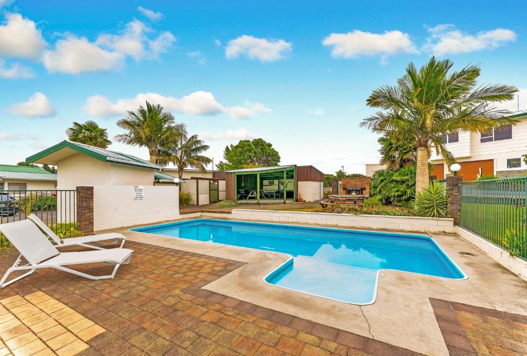 a swimming pool in a yard with a chair and a house at Cottage Park Thermal Motel in Tauranga