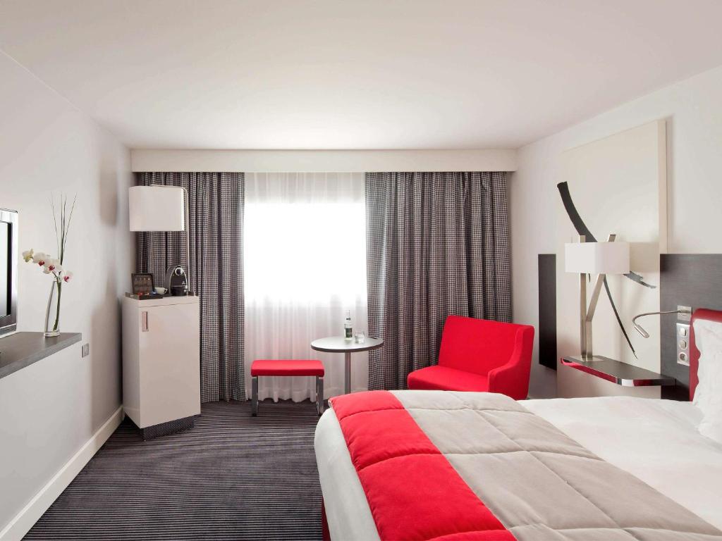 a hotel room with a bed and a red chair at Mercure Paris CDG Airport & Convention in Roissy-en-France