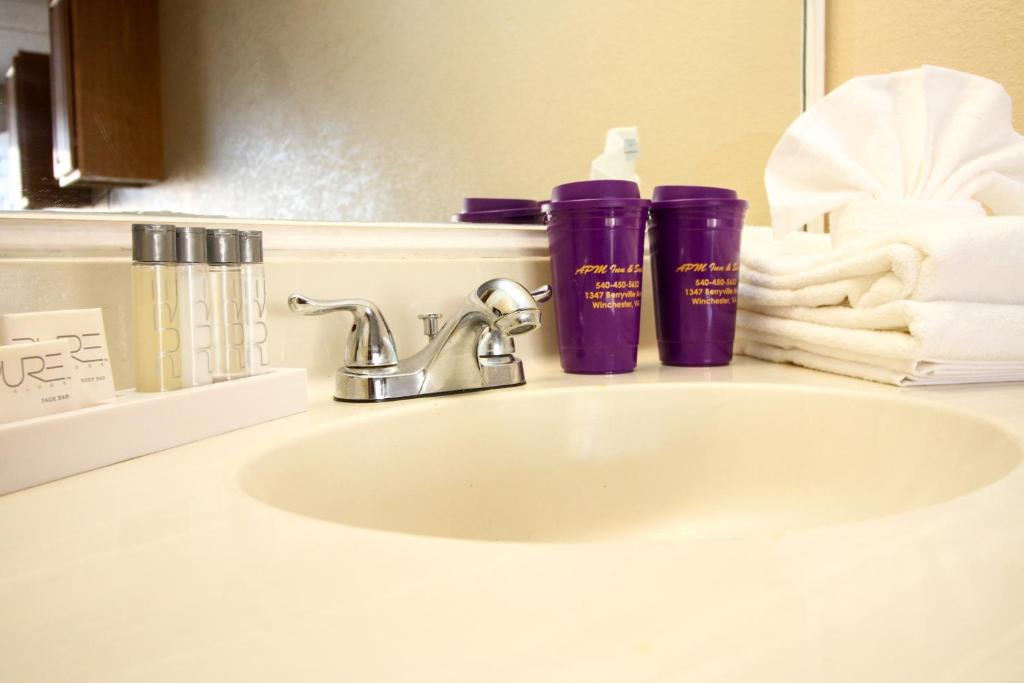 a bathroom sink with two purple cups and towels at APM Inn and Suites in Winchester