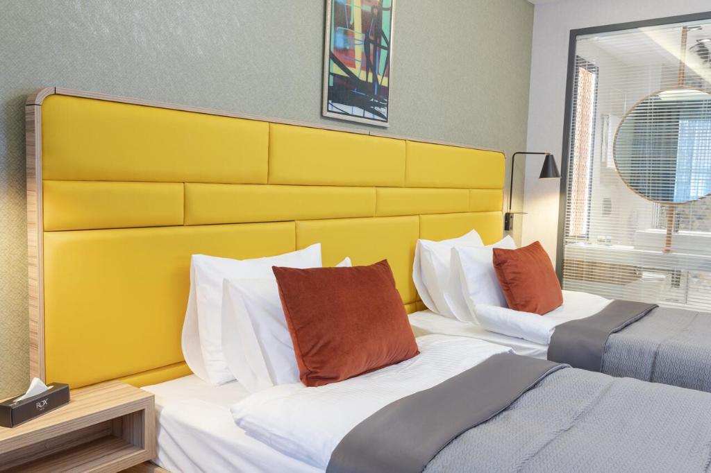 two beds in a bedroom with a yellow headboard at ROX Hotel Ankara in Ankara