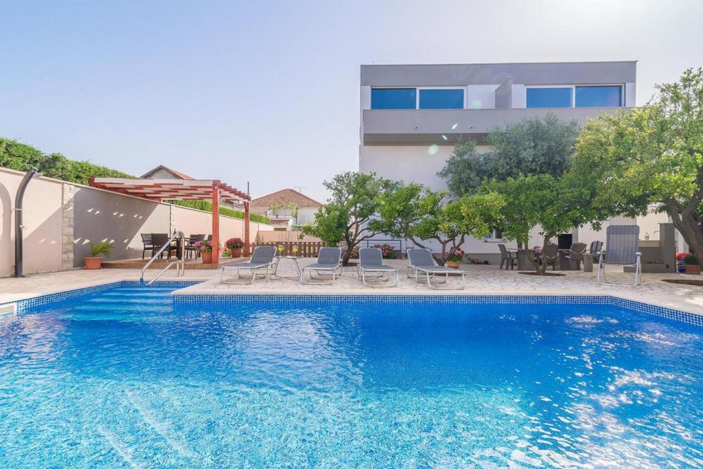 een groot blauw zwembad met stoelen en een gebouw bij Apartments Villa Odesa with shared pool in Zadar