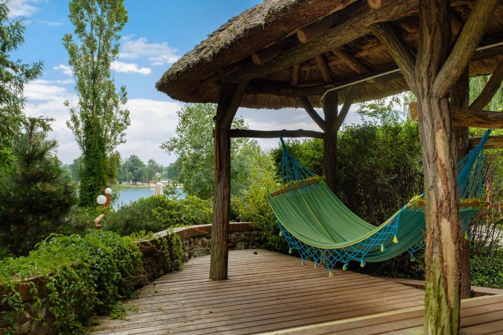 Wooden gazebo with hammock overlooking a serene lake and lush greenery.