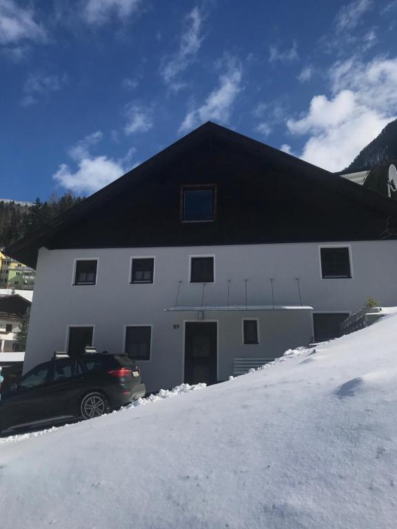 a white building with a black roof in the snow at Landhaus Pitztal inklusive Sommercard in Jerzens