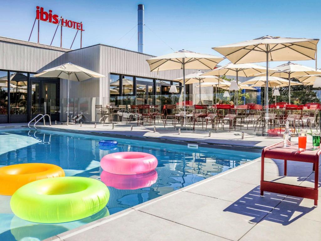 a swimming pool with colorful chairs and umbrellas at ibis Orange Centre in Orange