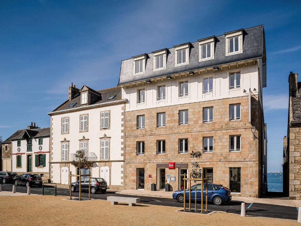 un grand bâtiment avec des voitures garées devant lui dans l'établissement ibis Roscoff, à Roscoff