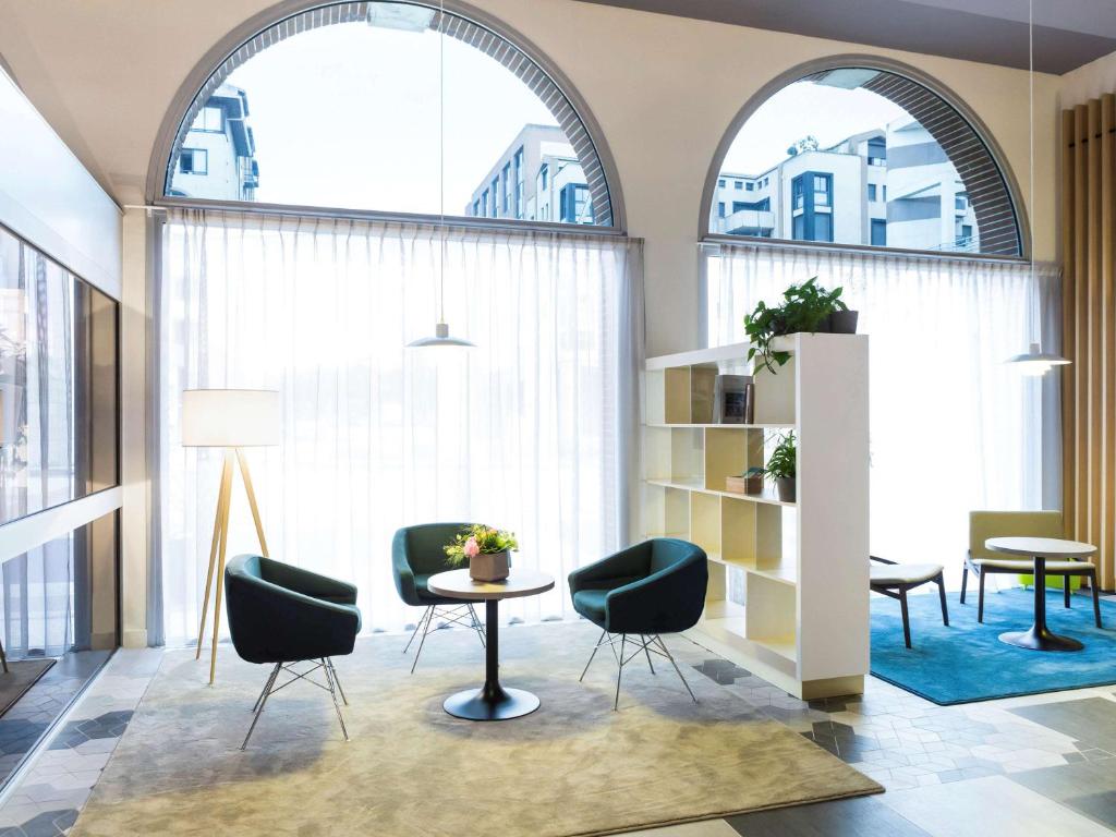 トゥールーズにあるノボテル トゥールーズ サントル コンパン カッファレッリのアーチ型の窓2つ、テーブルと椅子が備わるロビー