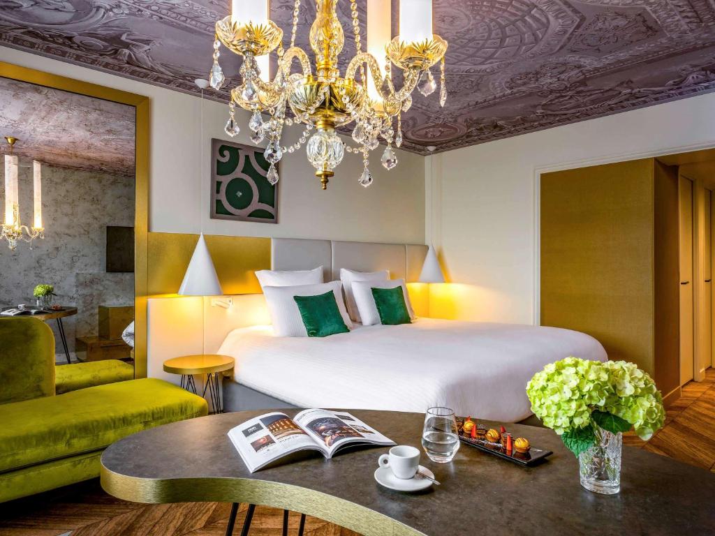 Un dormitorio con una cama grande y una lámpara de araña. en Mgallery Le Louis Versailles Château, en Versalles