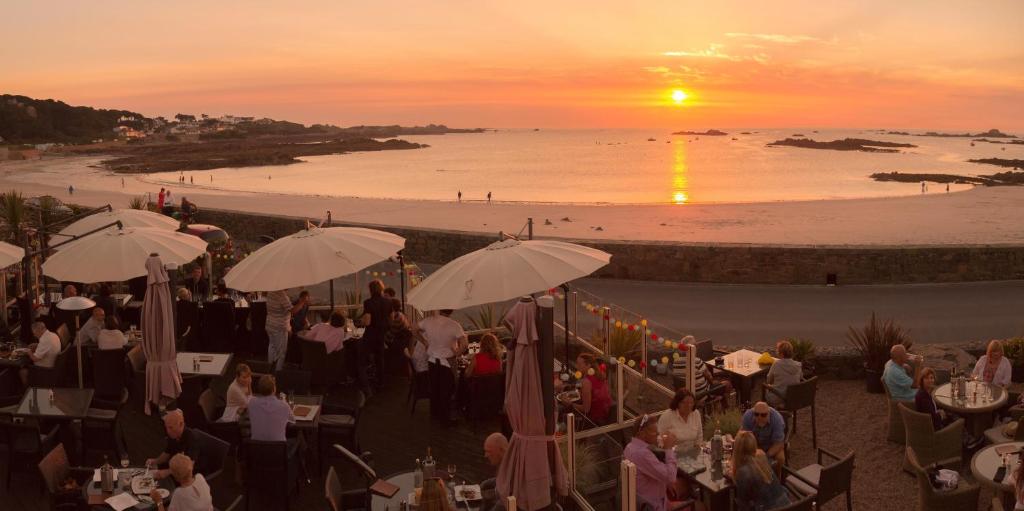 un gruppo di persone seduti ai tavoli sulla spiaggia al tramonto di Cobo Bay Hotel a Castel