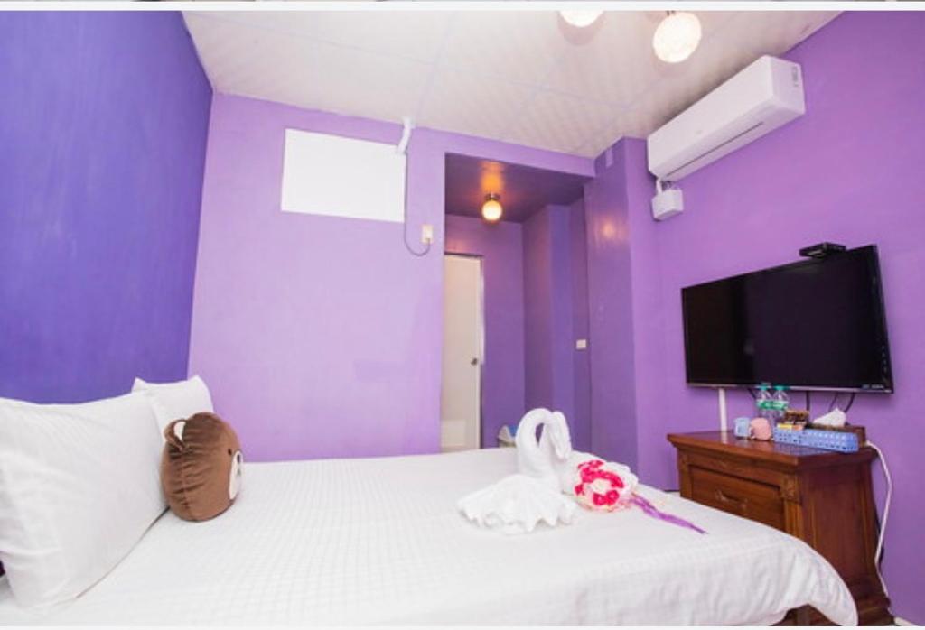 um quarto com paredes roxas e uma cama com uma televisão em Happy Homestay em Budai