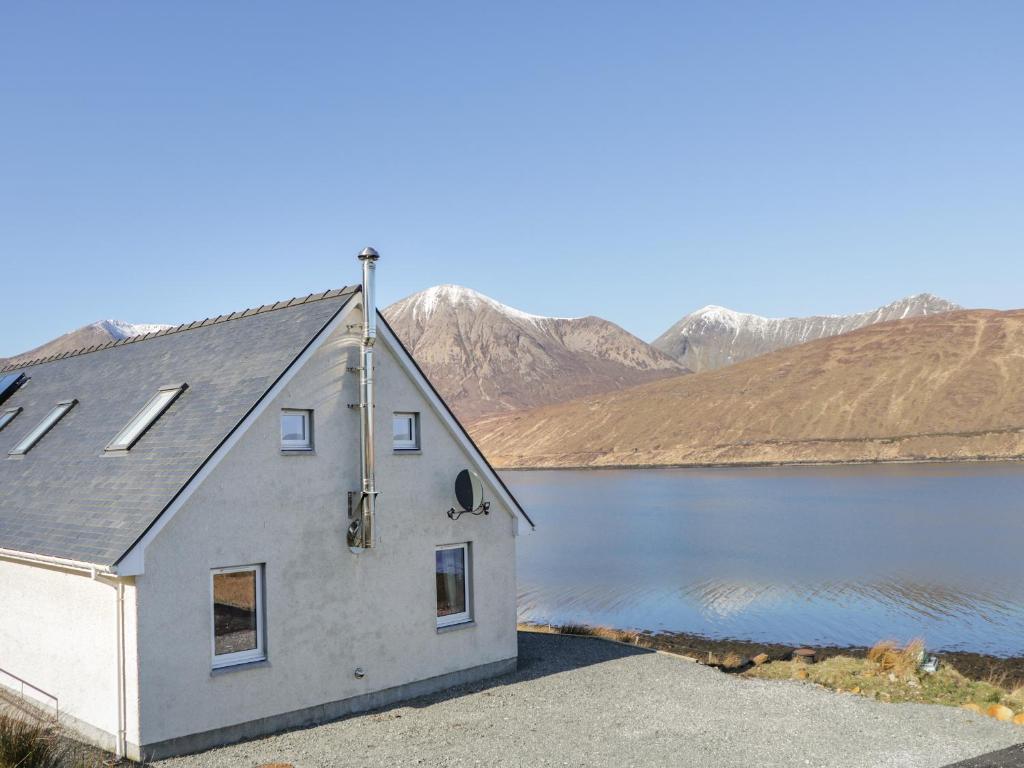 a house on a lake with mountains in the background at Cuillin Shores in Luib