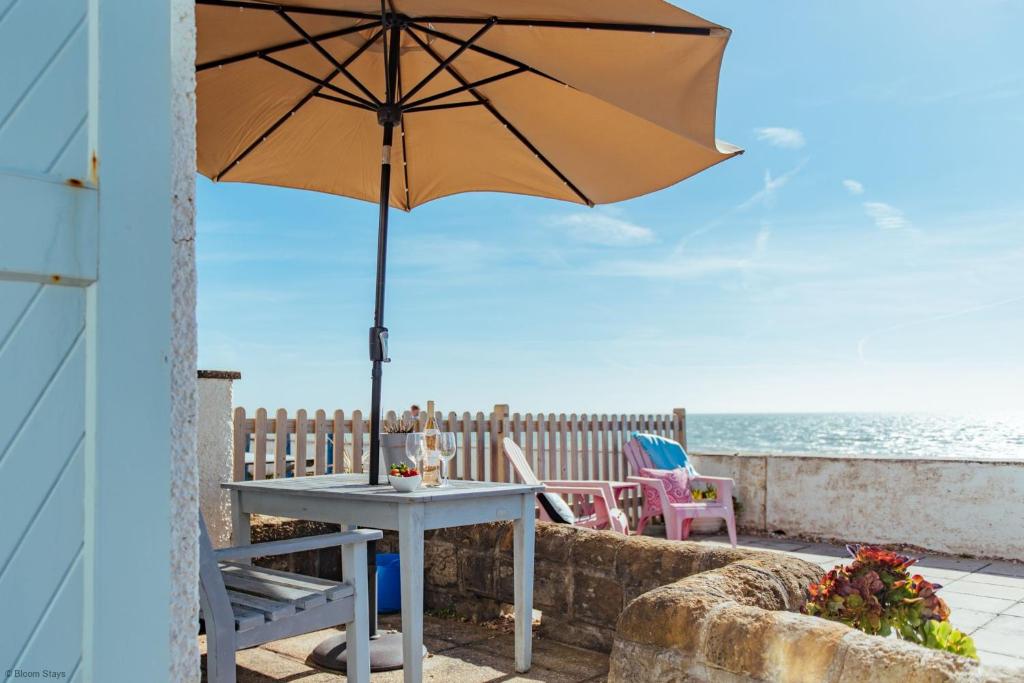 Driftwood Cottage by Bloom Stays في فولكستون: طاولة مع مظلة على فناء يطل على المحيط