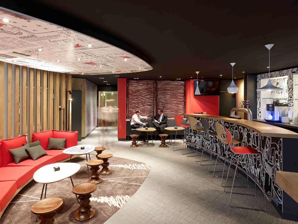 a lobby with red furniture and two people sitting at tables at ibis Köln Centrum in Cologne