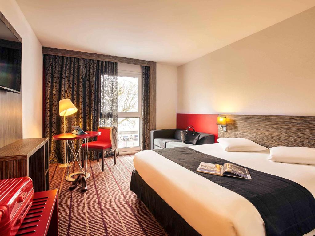 ブロワにあるホテル メルキュール ブロワ サントルの大きなベッドとデスクが備わるホテルルームです。