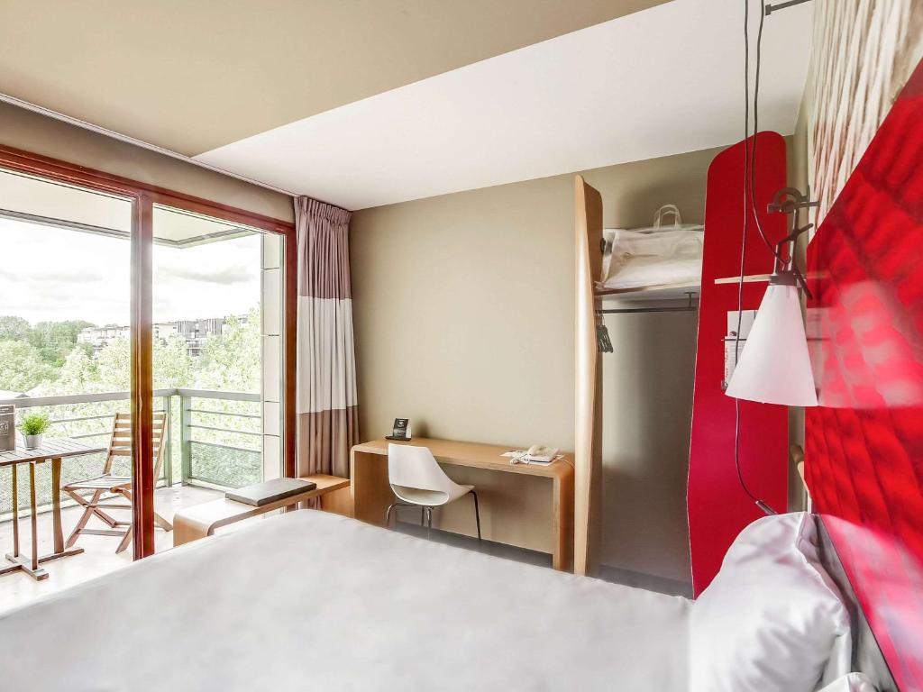 a hotel room with a bed and a desk and a balcony at ibis Paris Bercy Village in Paris