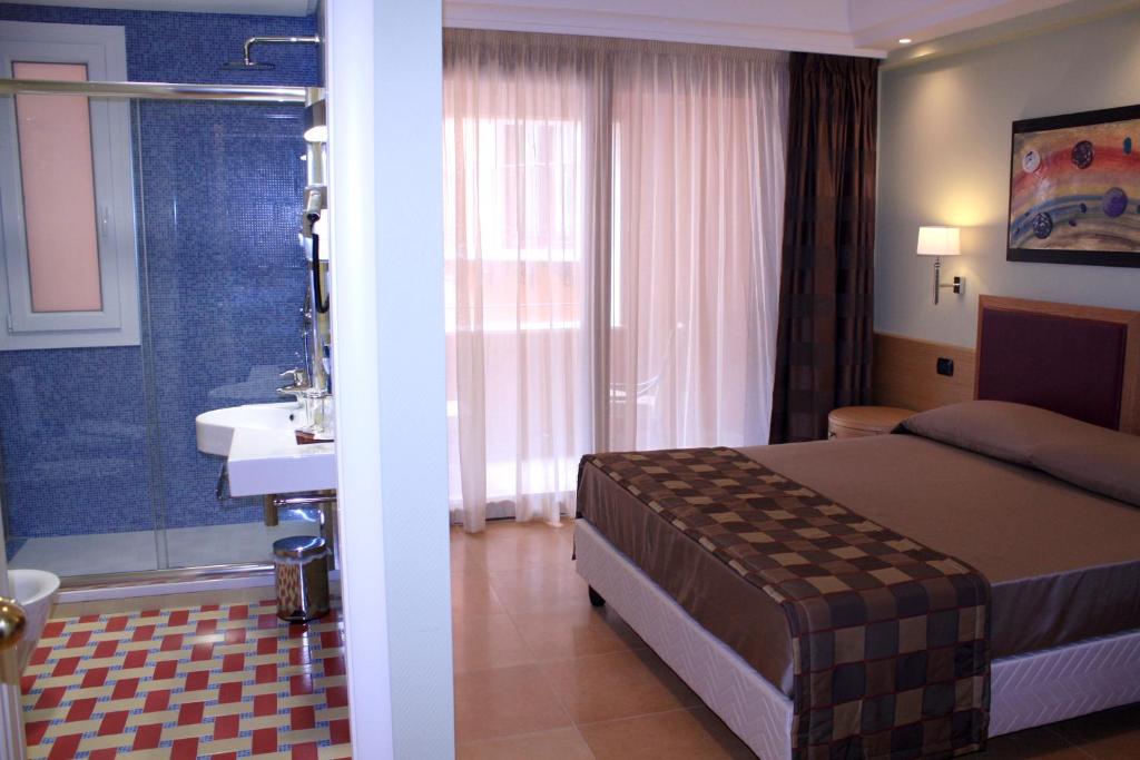 a bedroom with a bed and a bathroom with a sink at Artemis Hotel in Cefalù