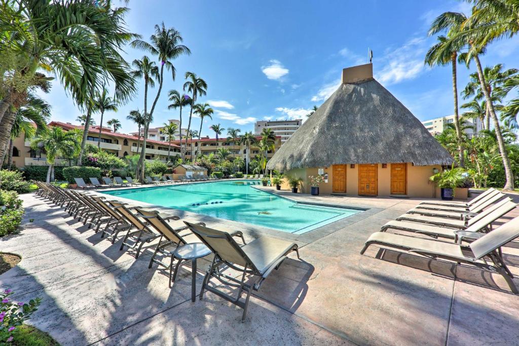 a pool with lounge chairs and a thatched building at Marina Sol Los Cabos Haven - Walk to Medano Beach! in Cabo San Lucas