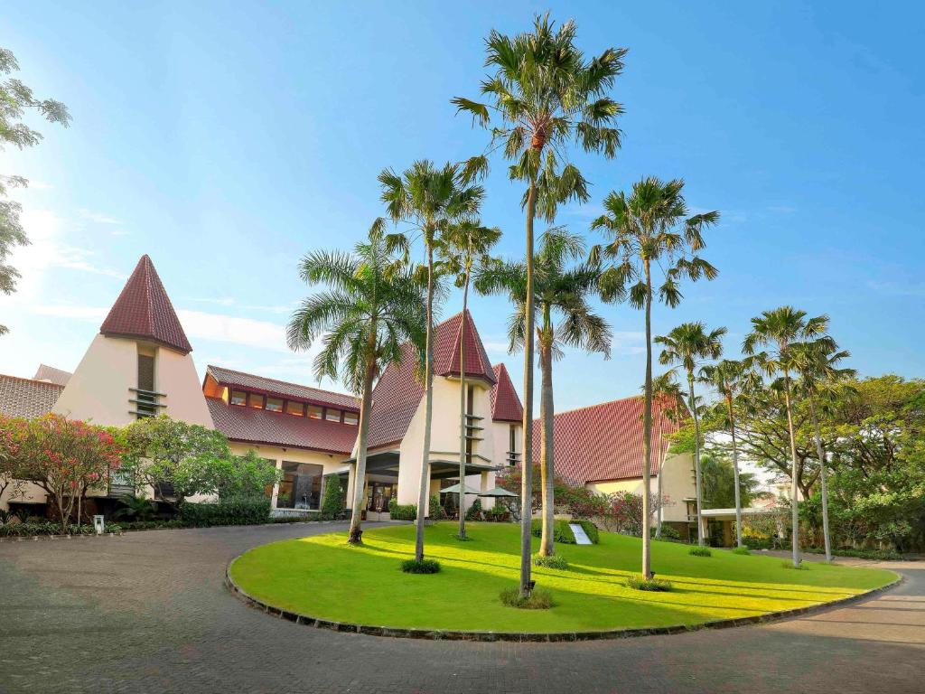 a resort with palm trees in front of a building at Grand Tropic Suites Hotel Surabaya in Surabaya