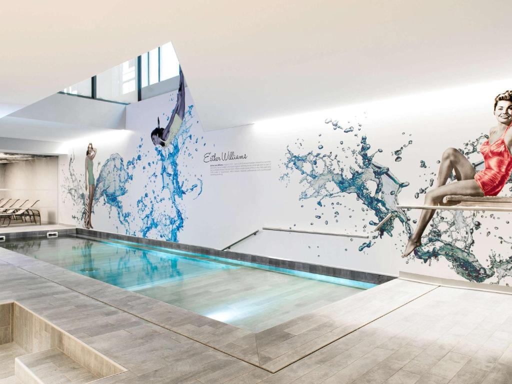 a swimming pool mural in a building with a woman sitting on a chair at Novotel Brussels City Centre in Brussels