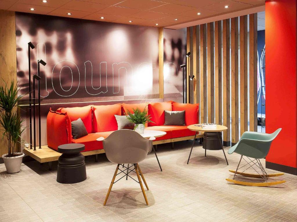 a lobby with an orange couch and tables and chairs at ibis Cherbourg La Glacerie in Cherbourg en Cotentin