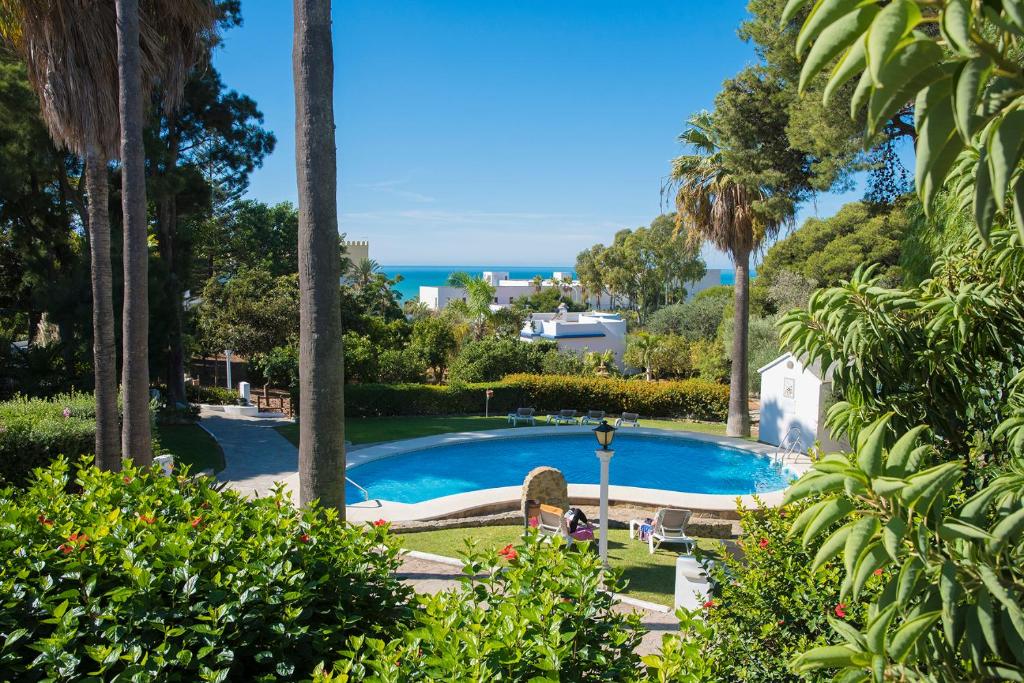 una piscina con palmeras y el océano en Suites Cortijo Fontanilla, en Conil de la Frontera