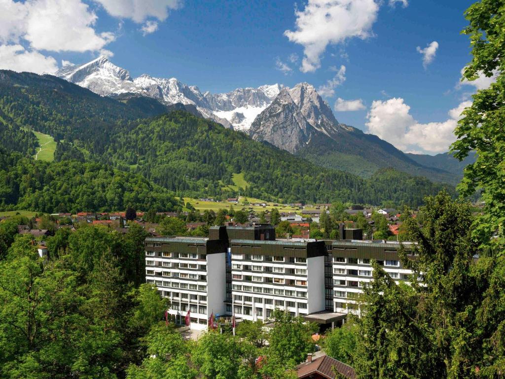 ein Gebäude vor einer Bergkette mit Bäumen in der Unterkunft Mercure Hotel Garmisch Partenkirchen in Garmisch-Partenkirchen