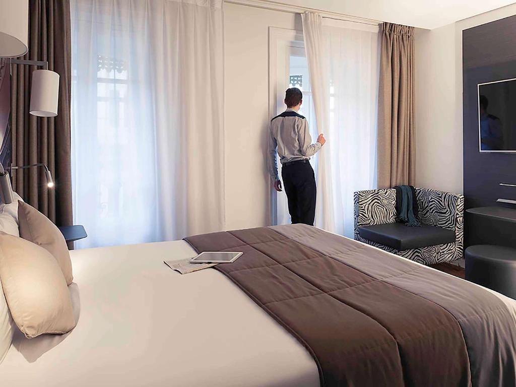 a man standing in a hotel room looking out the window at Mercure Lyon Centre Beaux-Arts in Lyon