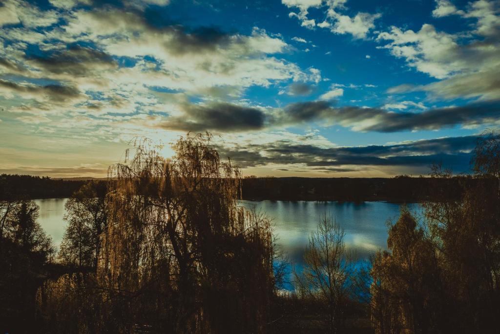 Lake view at sunset with silhouetted trees and dramatic clouds.