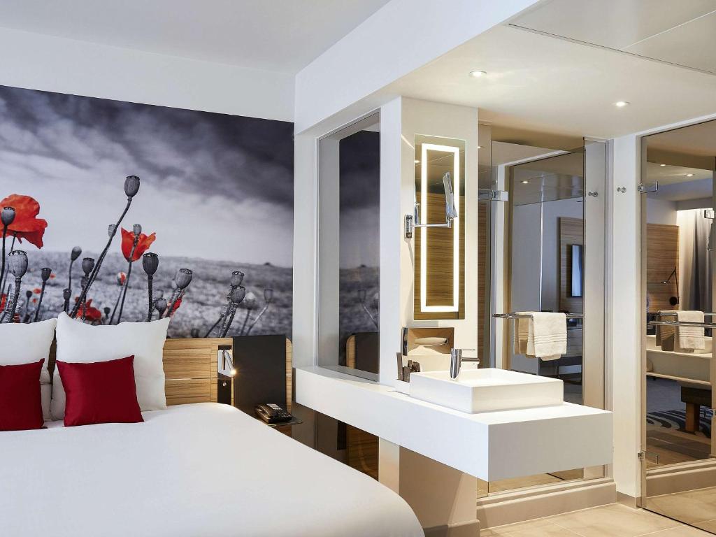 a bedroom with a large white bed and a bathroom at Novotel Ieper Centrum in Ypres