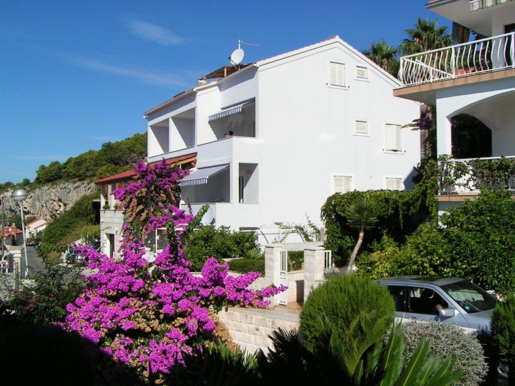 un edificio blanco con flores púrpuras delante de él en Apartments Viskovic Margita en Hvar