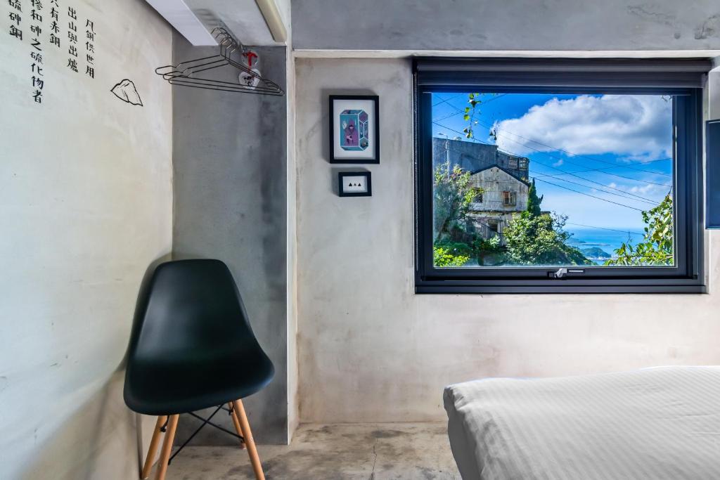 a bedroom with a window and a black chair at H&amp; Jiufen Ore Inn in Jiufen