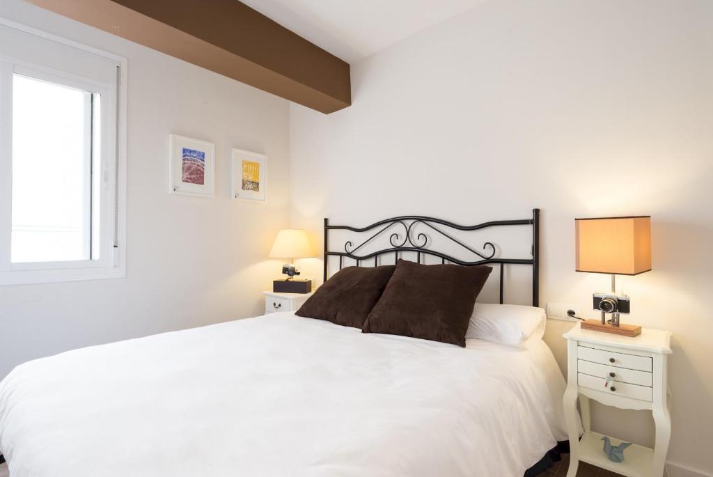 a bedroom with a white bed with two lamps and a window at MalagaSuite Historic City Centre in Málaga