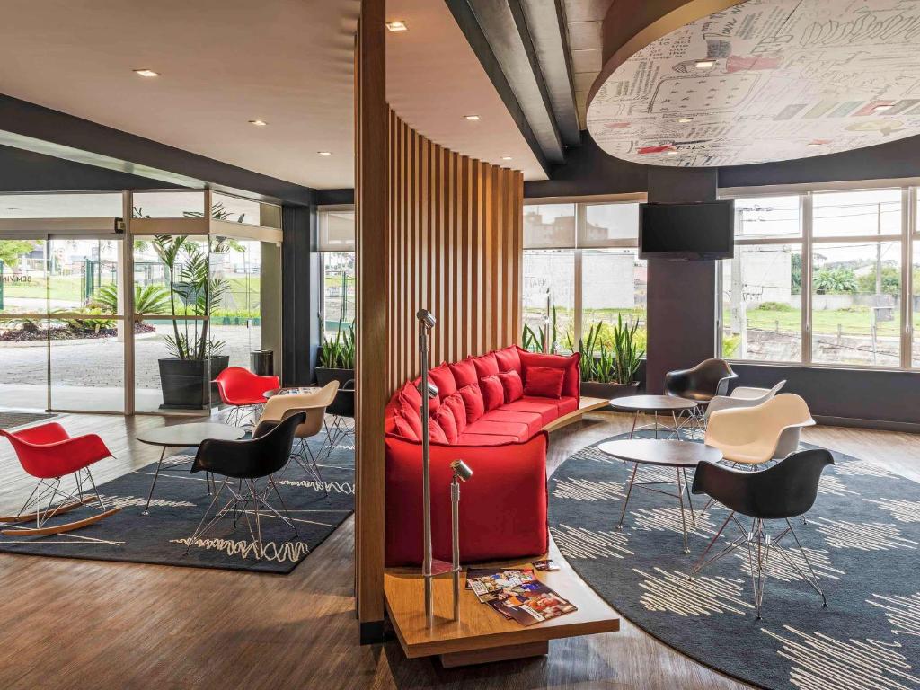 eine Lobby mit einem roten Sofa sowie Tischen und Stühlen in der Unterkunft ibis Curitiba Aeroporto in São José dos Pinhais
