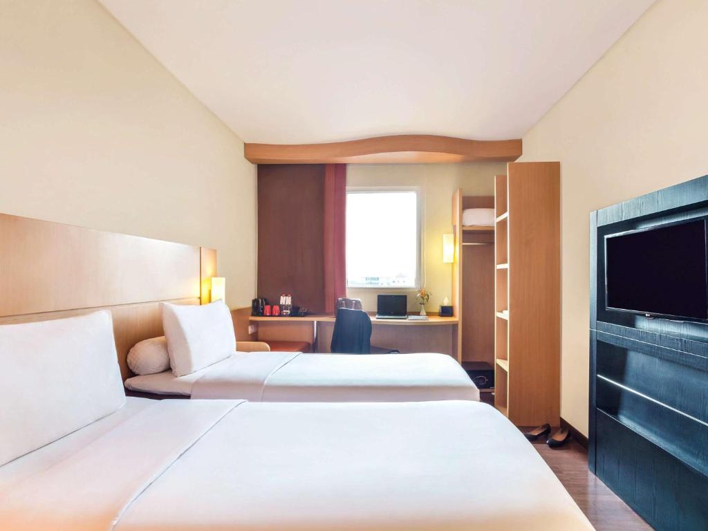 um quarto de hotel com duas camas e uma televisão de ecrã plano em Ibis Surabaya City Center em Surabaia