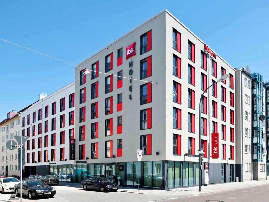 a large white building with red windows on a street at ibis München City Süd in Munich