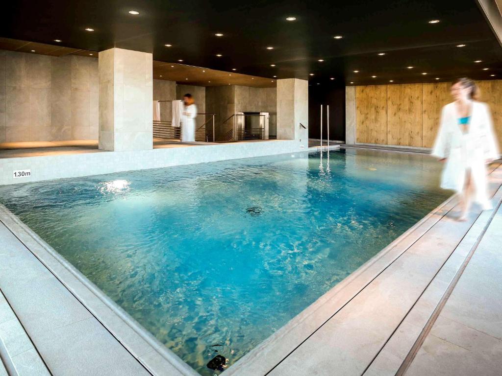 a woman walks past a swimming pool in a hotel at Ibis Niort Est Mendes France in Niort