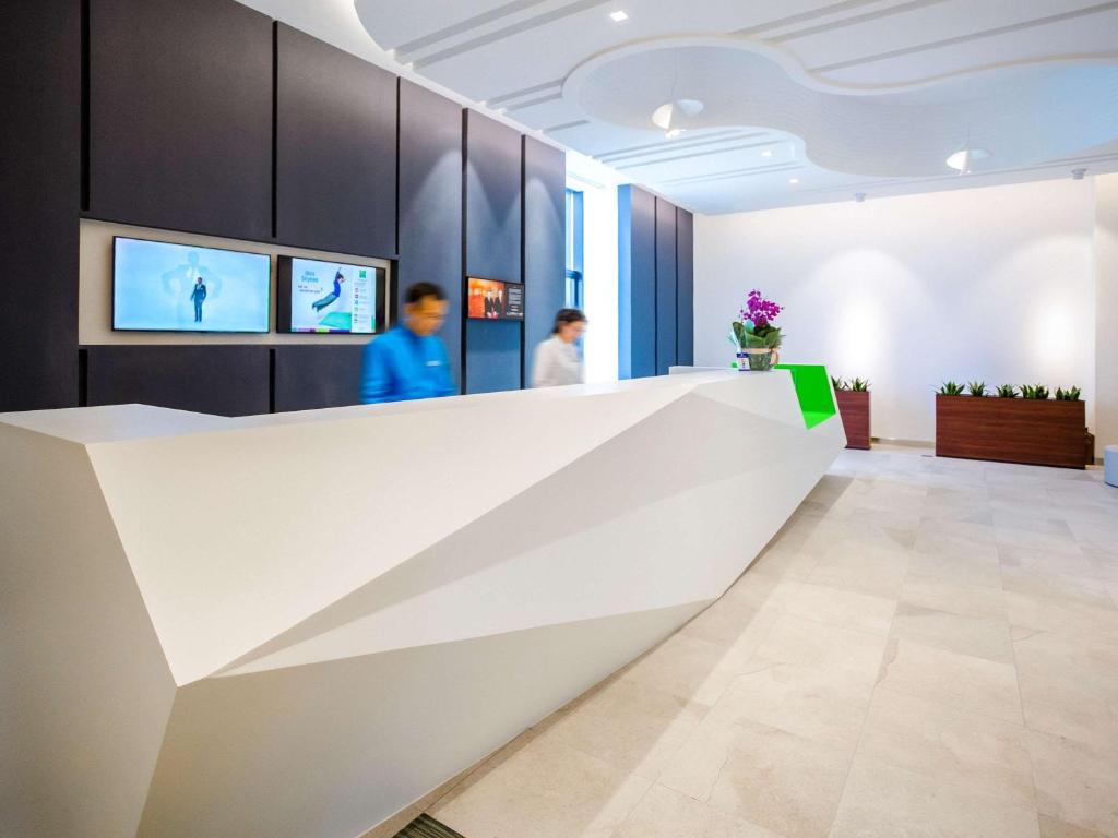 a reception desk in a lobby with two people in the background at IBIS Styles Ulaanbaatar Polaris in Ulaanbaatar