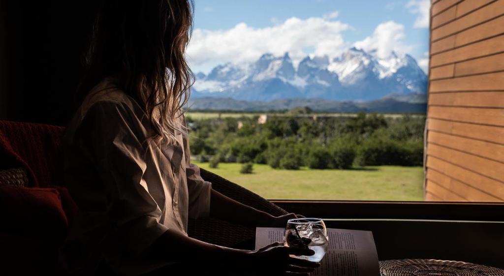 a woman holding a glass of wine looking out a window at Río Serrano Hotel + Spa in Torres del Paine