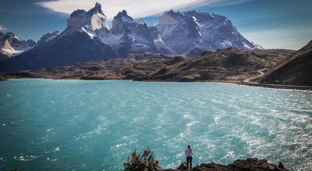 a person standing next to a body of water with a mountain at Río Serrano Hotel + Spa in Torres del Paine