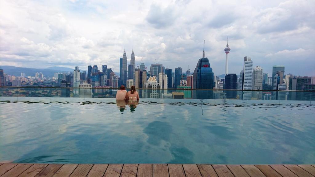 KLCC Regalia Suites Infinity Pool Kuala Lumpur في كوالالمبور: زوجين يقفان في مسبح لا متناهي مع إطلالة على المدينة