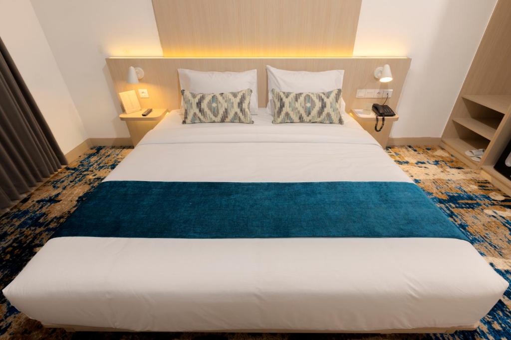 a bedroom with a large white bed with a blue blanket at Cordia Hotel Yogyakarta - Hotel Dalam Bandara in Glagah