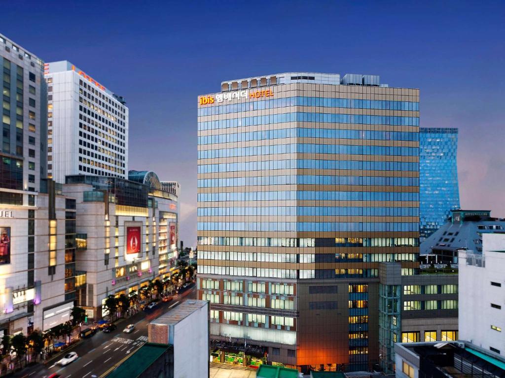 a tall glass building in a city with traffic at Ibis Ambassador Myeongdong in Seoul