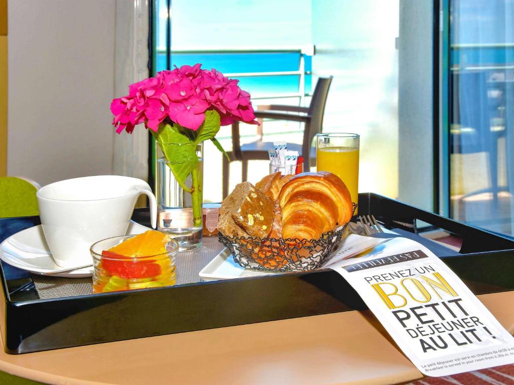 a table with a tray of food and flowers and a book at Mercure Granville Le Grand Large in Granville